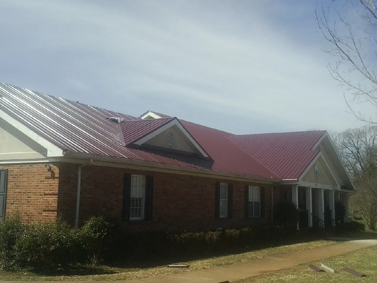 Red metal roof with gabled entries on a long brick building, from a Hail Damage Roof Repair job in Lilesville