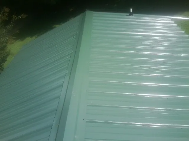 New green metal panels meeting at the ridge of a roof — Flat Roof Repair work by our crew in Lilesville