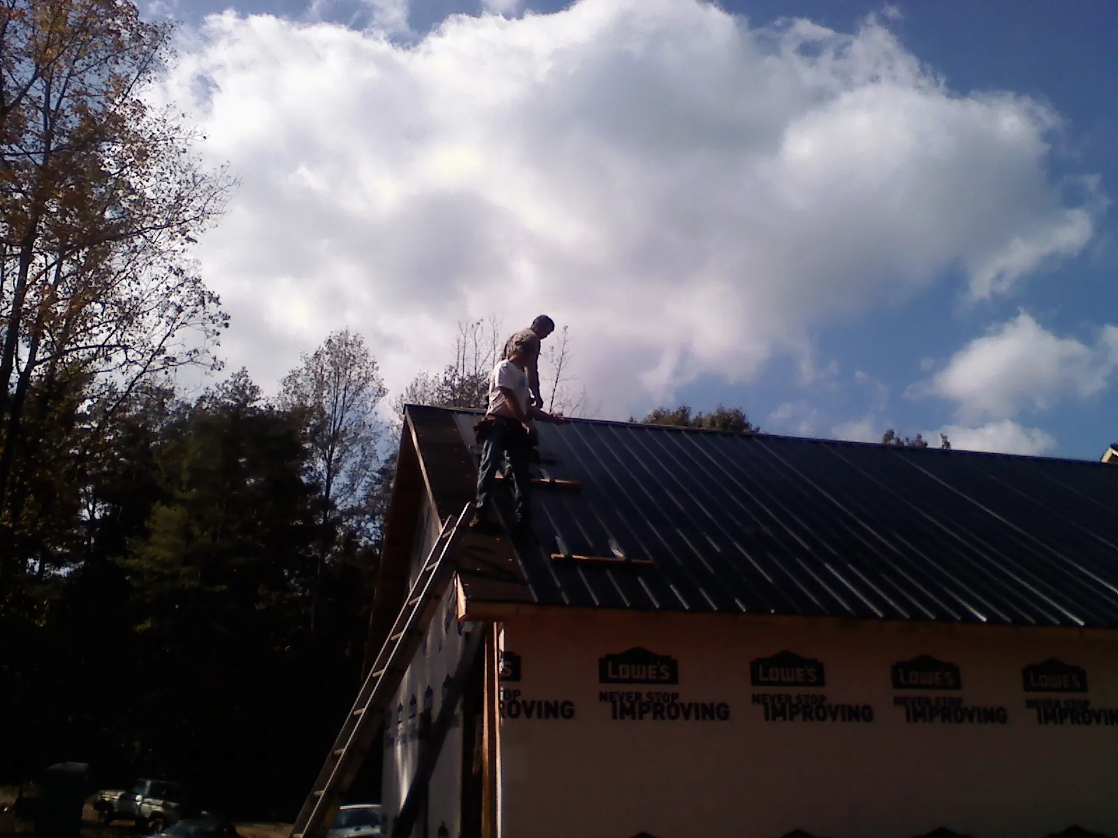 Roofer fastening dark metal panels high against a cloudy sky, from a Roof Inspection job in Lilesville