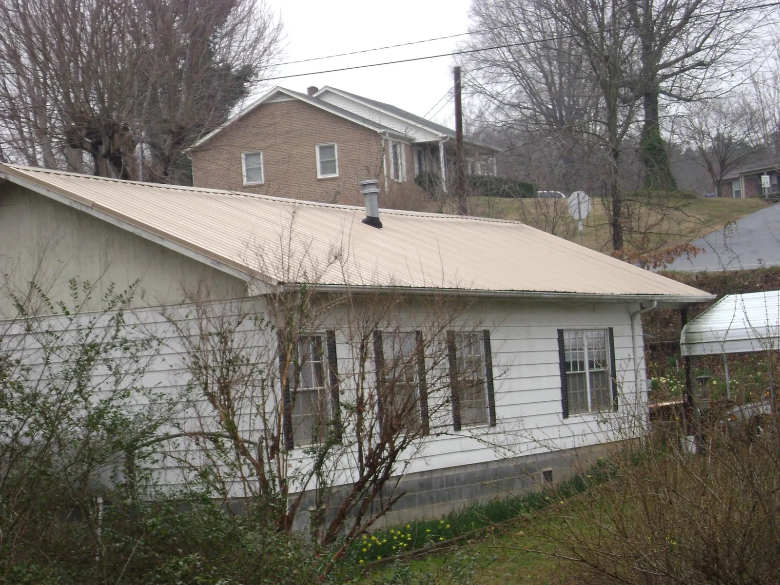 Tan metal roof on a white sided house set into a hillside — Commercial Roofing by Roofing Brothers in Lilesville