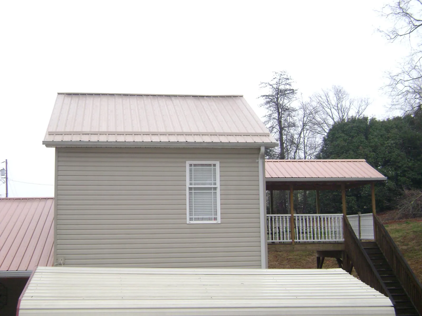 Tan metal roofs on a two story addition and attached porch, from a Roof Replacement job in Lilesville